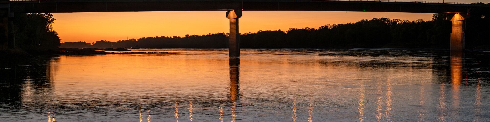 Un puente sobre un río tranquilo al atardecer, con luces a lo largo del puente.
