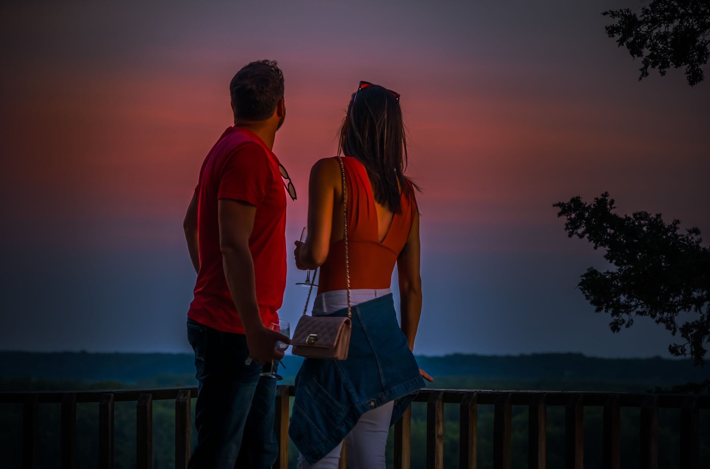 Young man and woman enjoying view of beautiful sunset from wooden deck overlooking Missouri River in summer; Missouri, Midwest