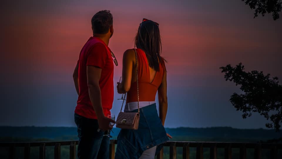 Young man and woman enjoying view of beautiful sunset from wooden deck overlooking Missouri River in summer; Missouri, Midwest