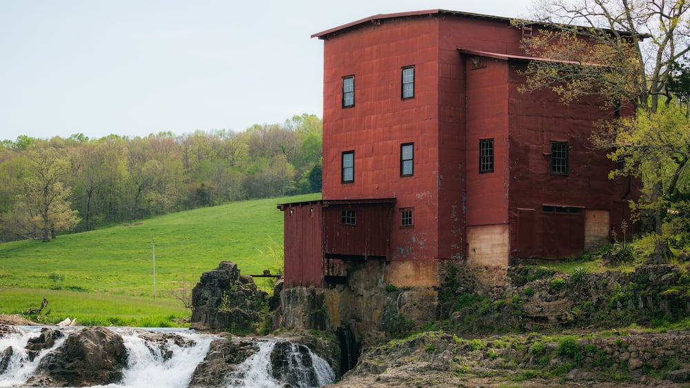 Eine rote Wassermühle neben einem Wasserfall in einem grünen Tal.
