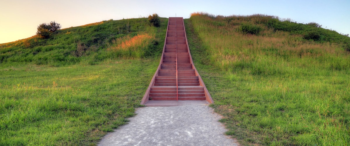 A long, narrow metal staircase ascending a grassy hill.