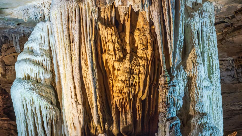 A cave with stalactites and stalagmites, illuminated by artificial lighting.