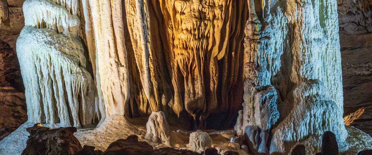 A cave with stalactites and stalagmites, illuminated by artificial lighting.
