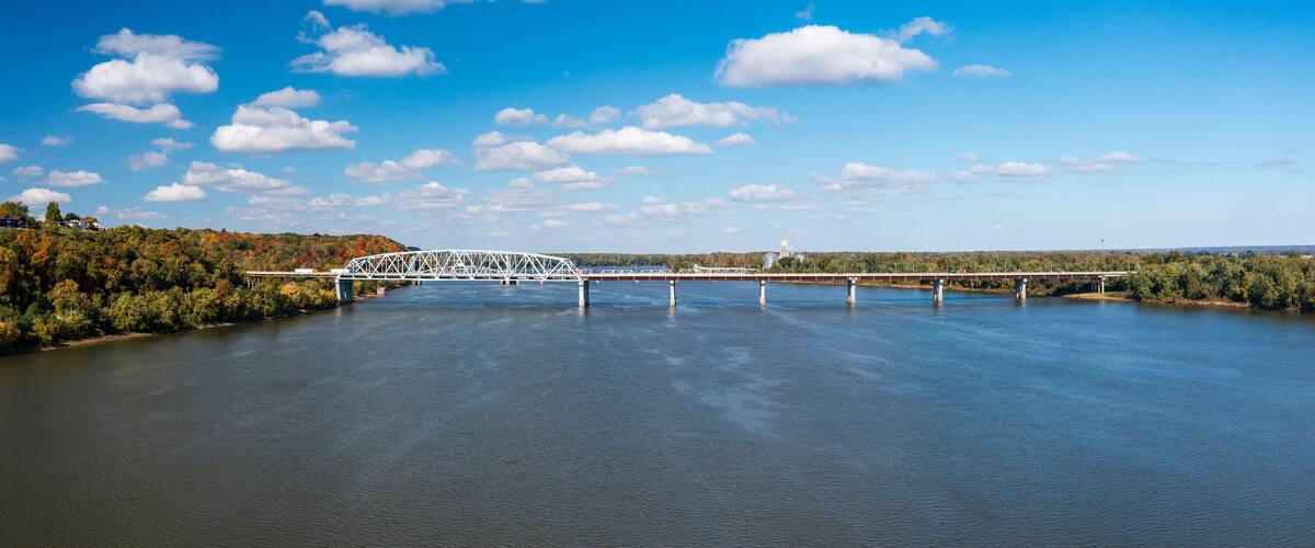 A white bridge over a calm river with trees and hills in the background.