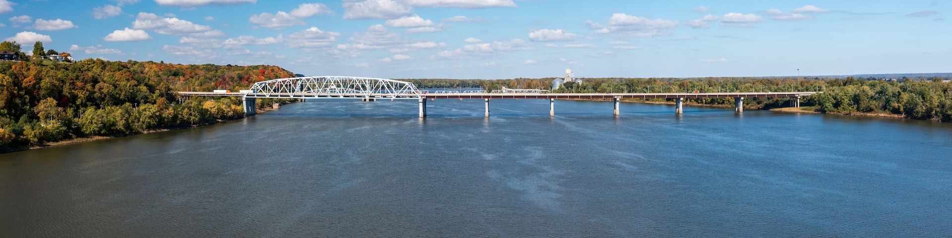 A white bridge over a calm river with trees and hills in the background.