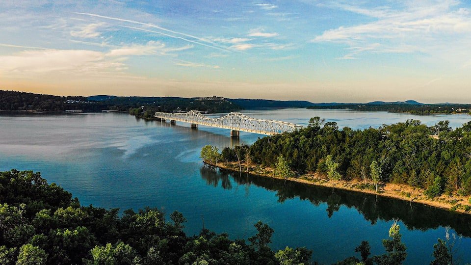 A bridge over a calm river surrounded by dense forests and distant hills.