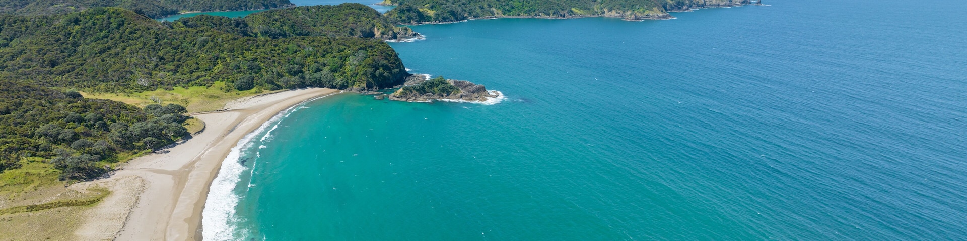 A coastal landscape with a sandy beach, turquoise waters, and green hills.