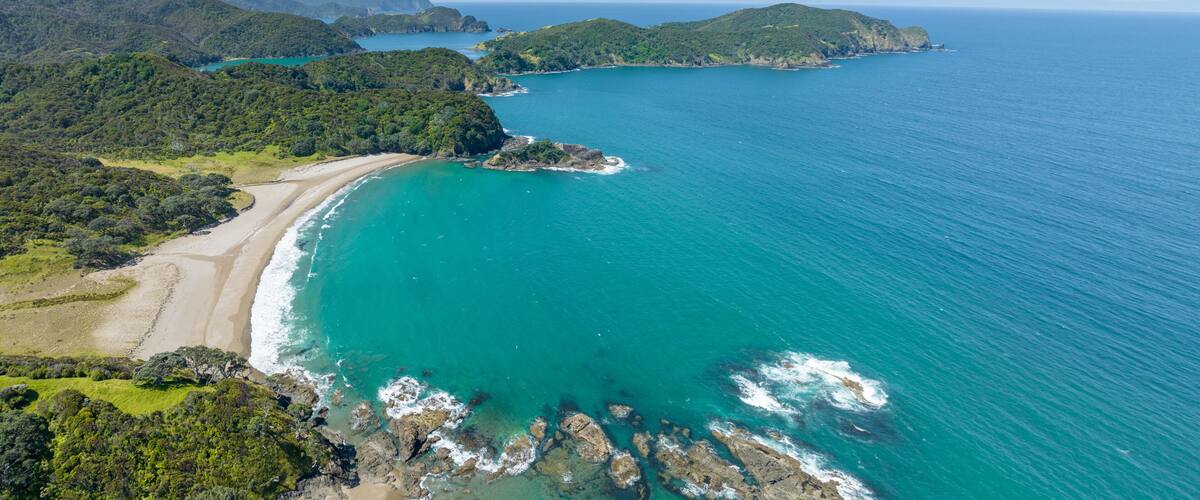 A coastal landscape with a beach, turquoise waters, and green hills.