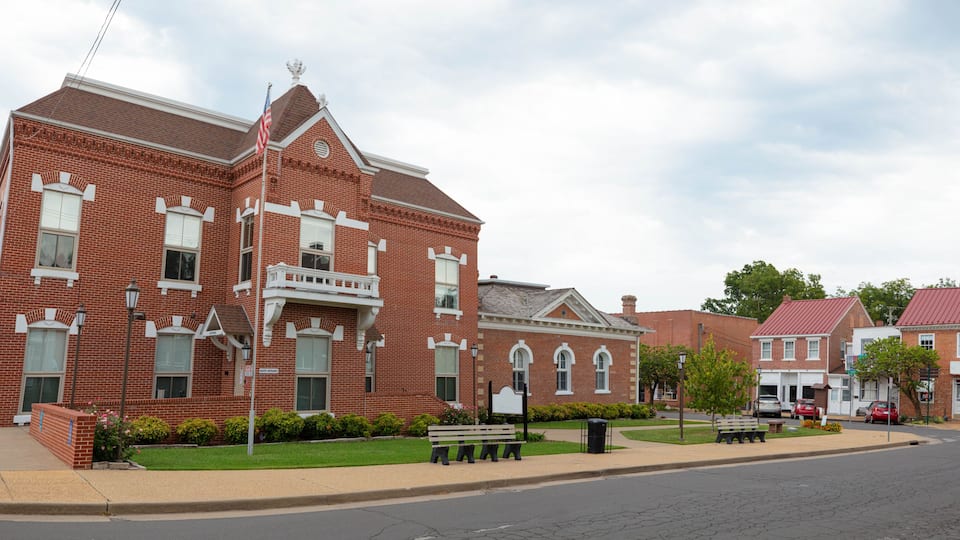 A red brick building with a white balcony, a street with benches, and a clear sky.