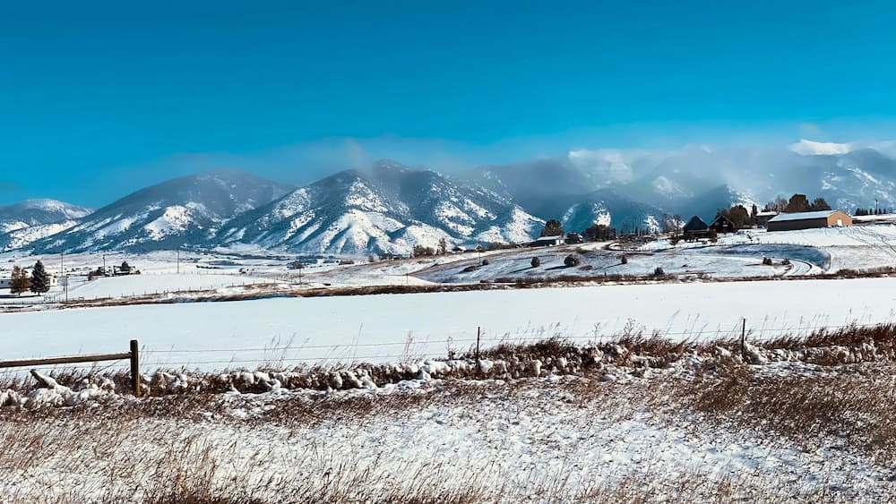A snow-covered landscape with mountains in the background and a few buildings.