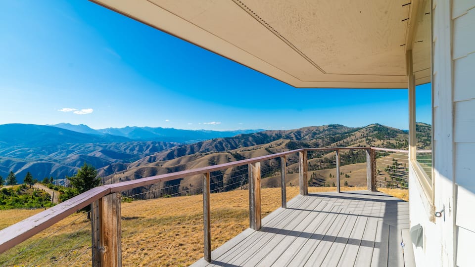 A wooden deck with a view of rolling hills and mountains under a clear blue sky.