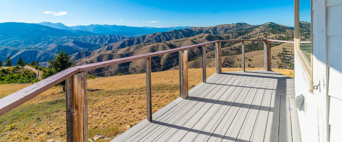 A wooden deck with a view of rolling hills and mountains under a clear blue sky.