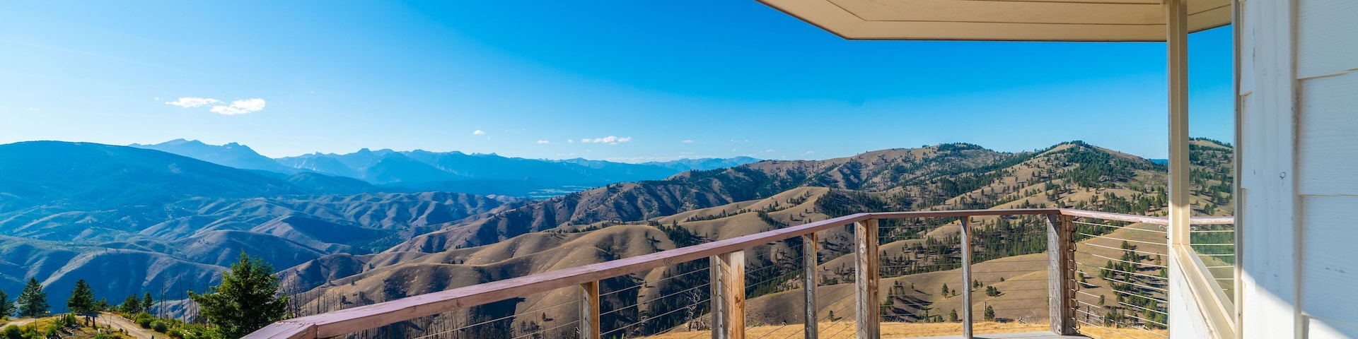 A wooden deck with a view of rolling hills and mountains under a clear blue sky.