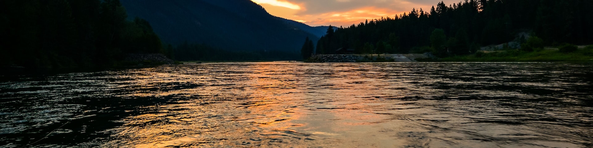 A river reflecting the sunset with mountains in the background.