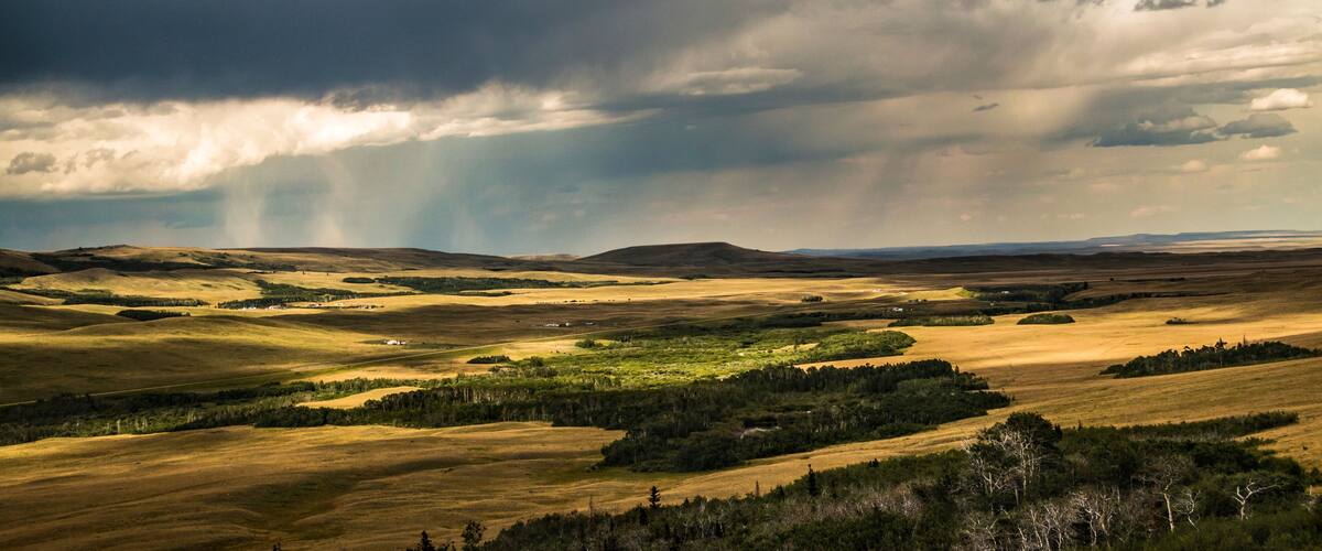 A vast landscape with rolling hills and a dramatic sky with clouds and sunlight.