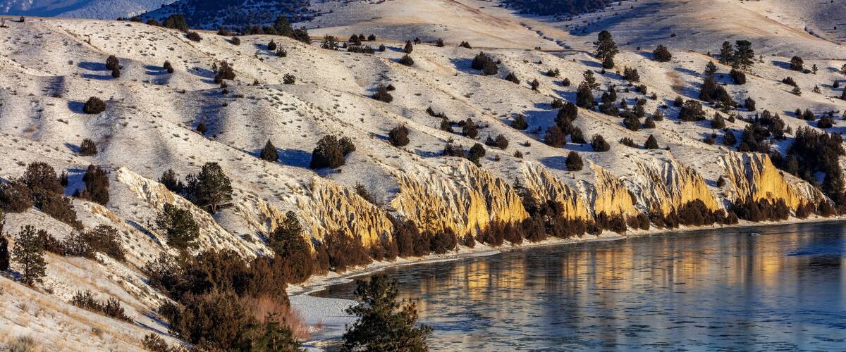A snow-covered landscape with mountains in the background and a river in the foreground.
