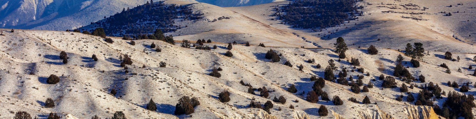 A snow-covered landscape with mountains in the background and a river in the foreground.
