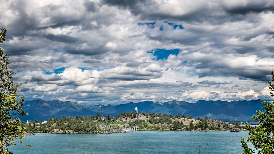 A lake with mountains in the background and a small town with houses and a church.
