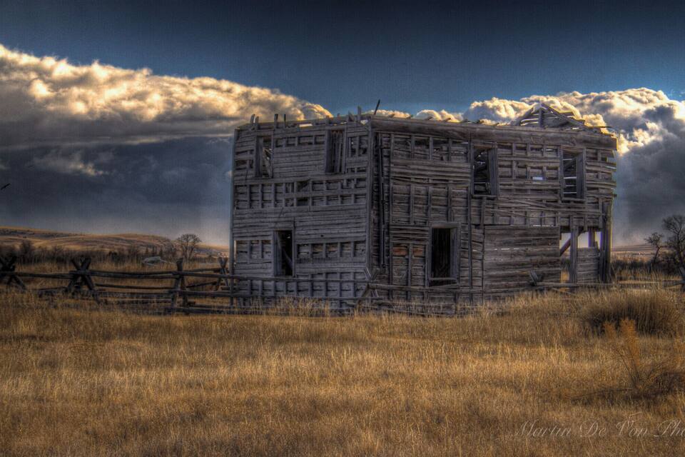 A dilapidated wooden structure in a grassy field with a dramatic sky.
