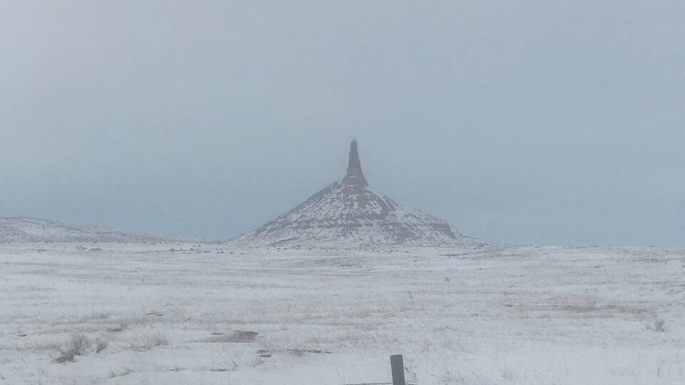 A snow-covered landscape with a prominent hill and a barbed wire fence in the foreground.