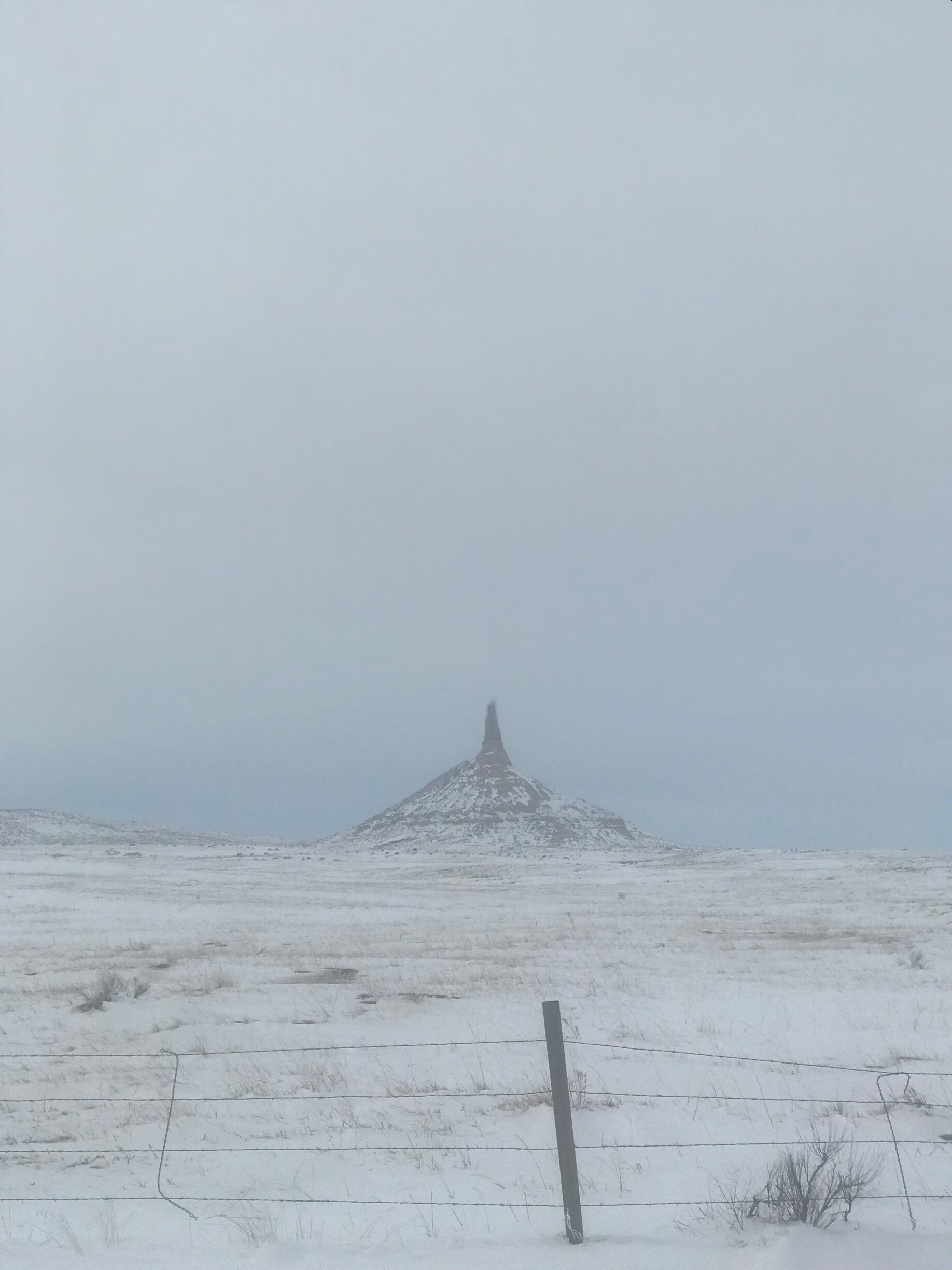 A snow-covered landscape with a prominent hill and a barbed wire fence in the foreground.