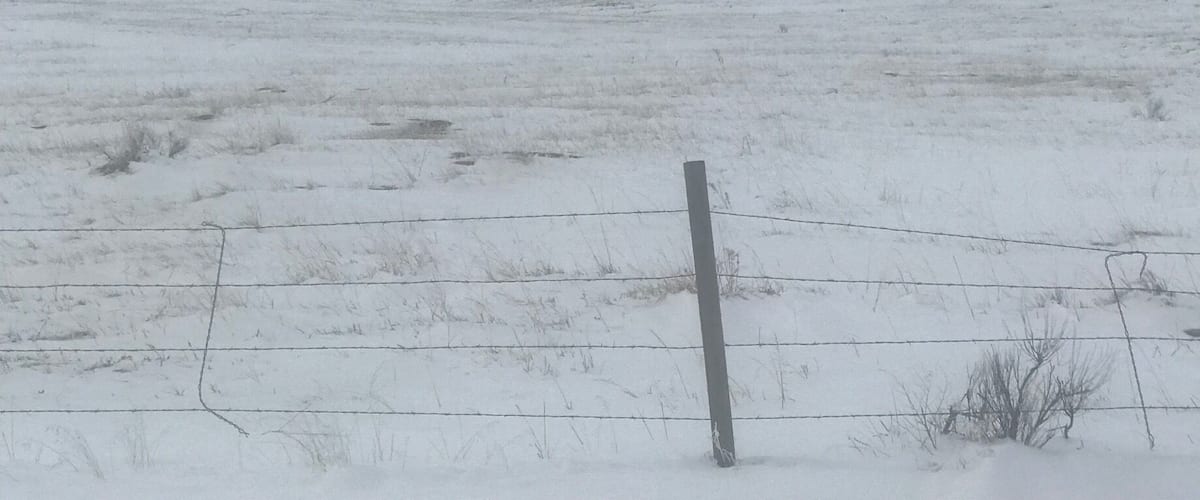 A snow-covered landscape with a prominent hill and a barbed wire fence in the foreground.
