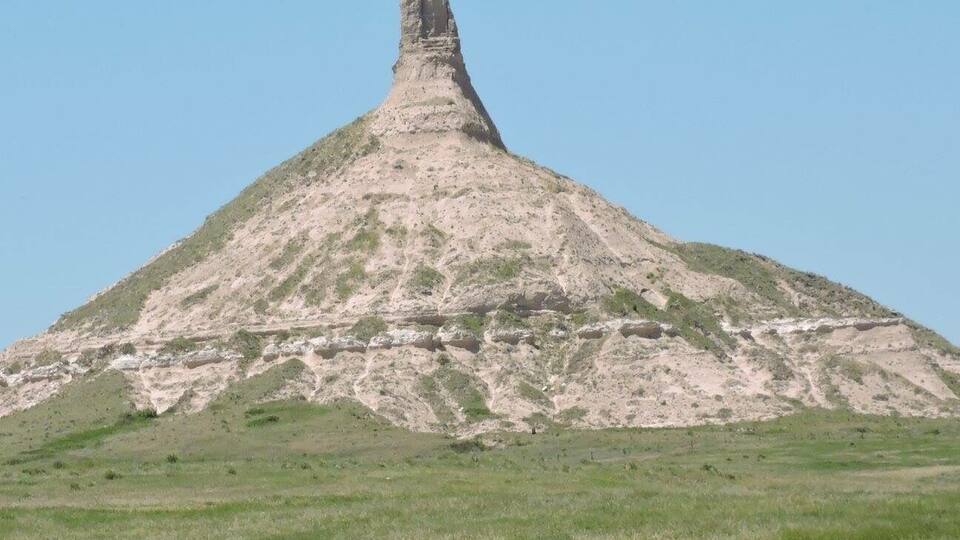 A large, conical hill with a narrow peak in a grassy field.