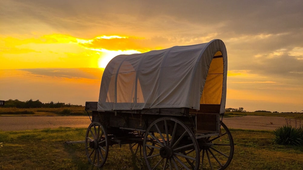 Ein beladener Wagen in einem Feld mit untergehender Sonne im Hintergrund.