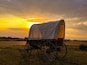 A covered wagon in a field with a sunset in the background.