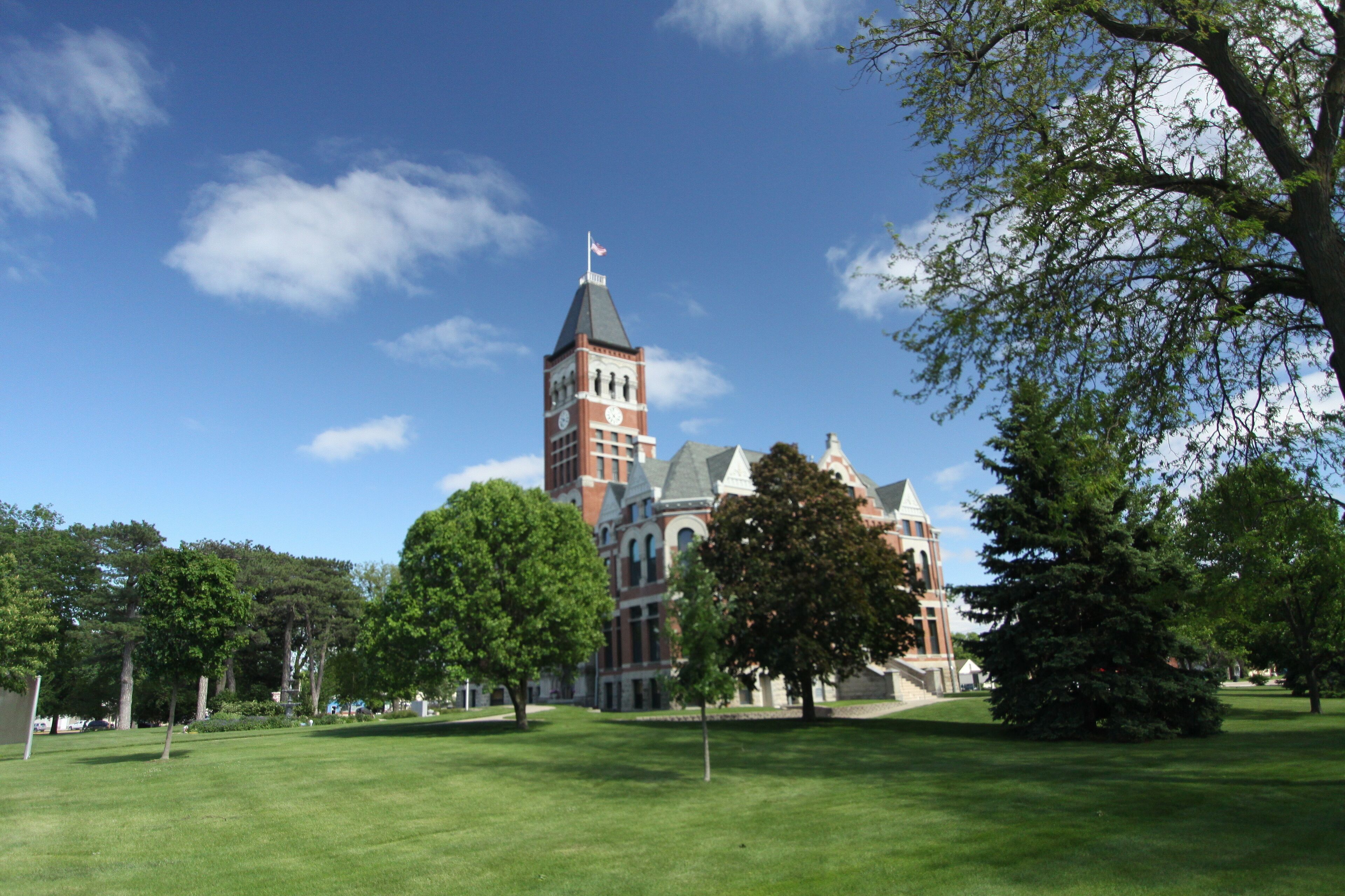 A large building with a tower and a flag, surrounded by green grass and trees.