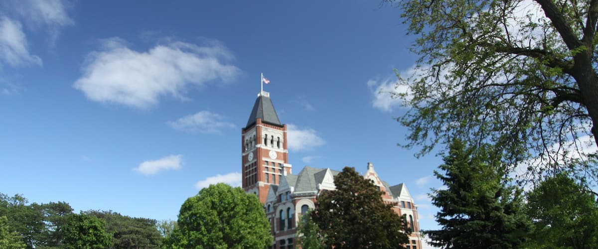 A large building with a tower and a flag, surrounded by green grass and trees.