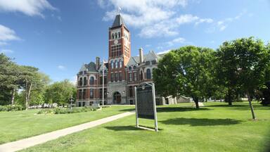 A historic building with a clock tower, surrounded by a well-maintained lawn and trees.