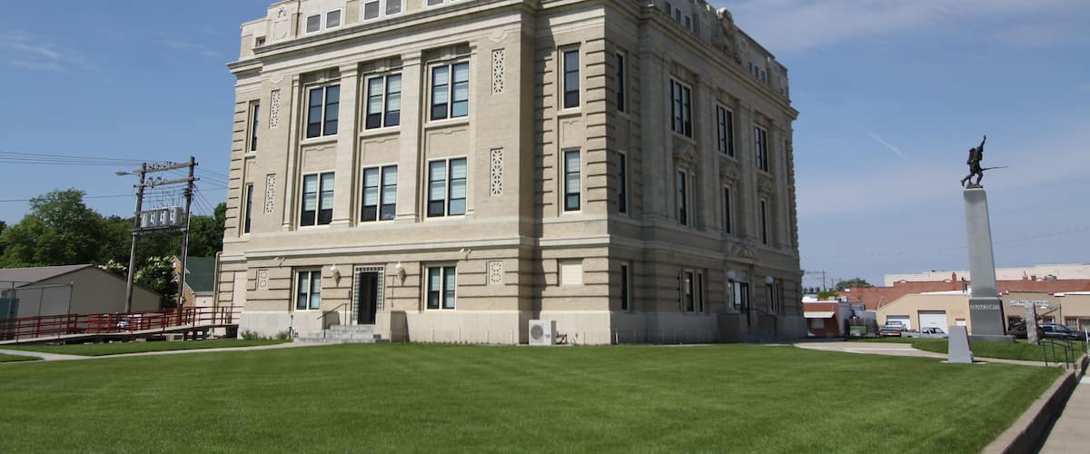 A large, beige building with a tall antenna on top, surrounded by a well-maintained lawn and a statue in the foreground.
