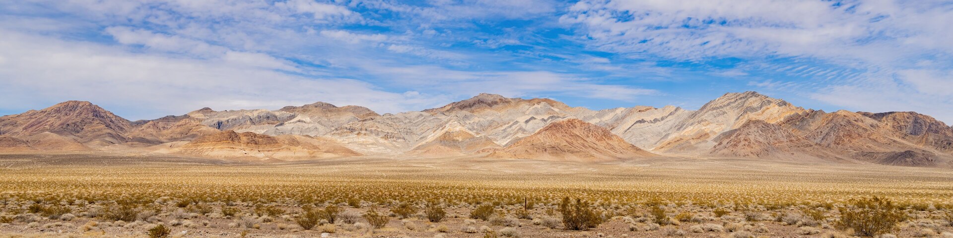 Paisaje desértico con vegetación escasa y una cadena de montañas bajo un cielo parcialmente nublado.