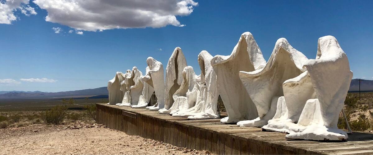 A row of white ice sculptures on a wooden platform in a desert landscape with mountains in the background.