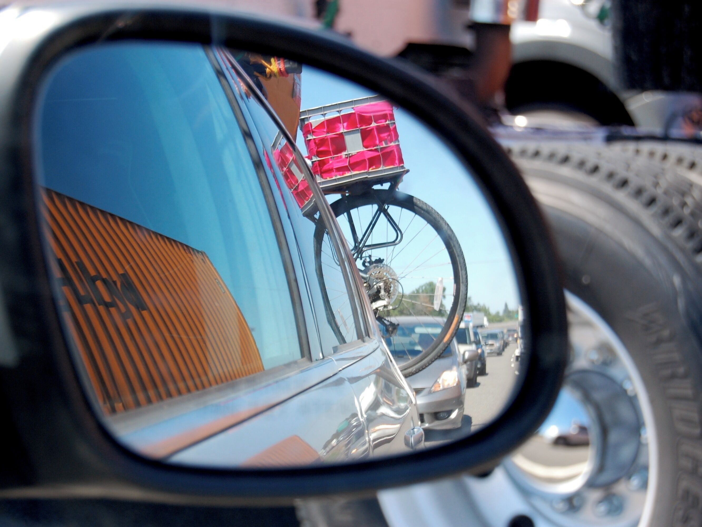 A side mirror reflection of a bicycle with a pink basket, a car's side mirror, and a tire.
