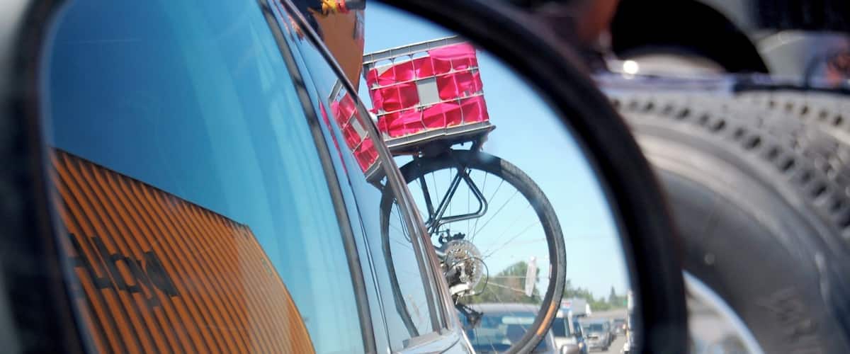 A side mirror reflection of a bicycle with a pink basket, a car's side mirror, and a tire.