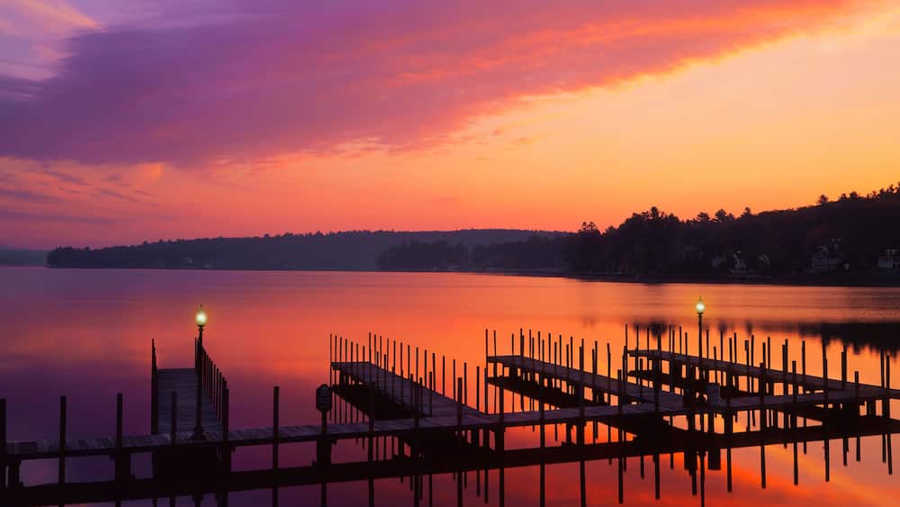 Un coucher de soleil sur un lac paisible, avec une jetée et une plateforme en bois qui s’avancent dans l’eau.