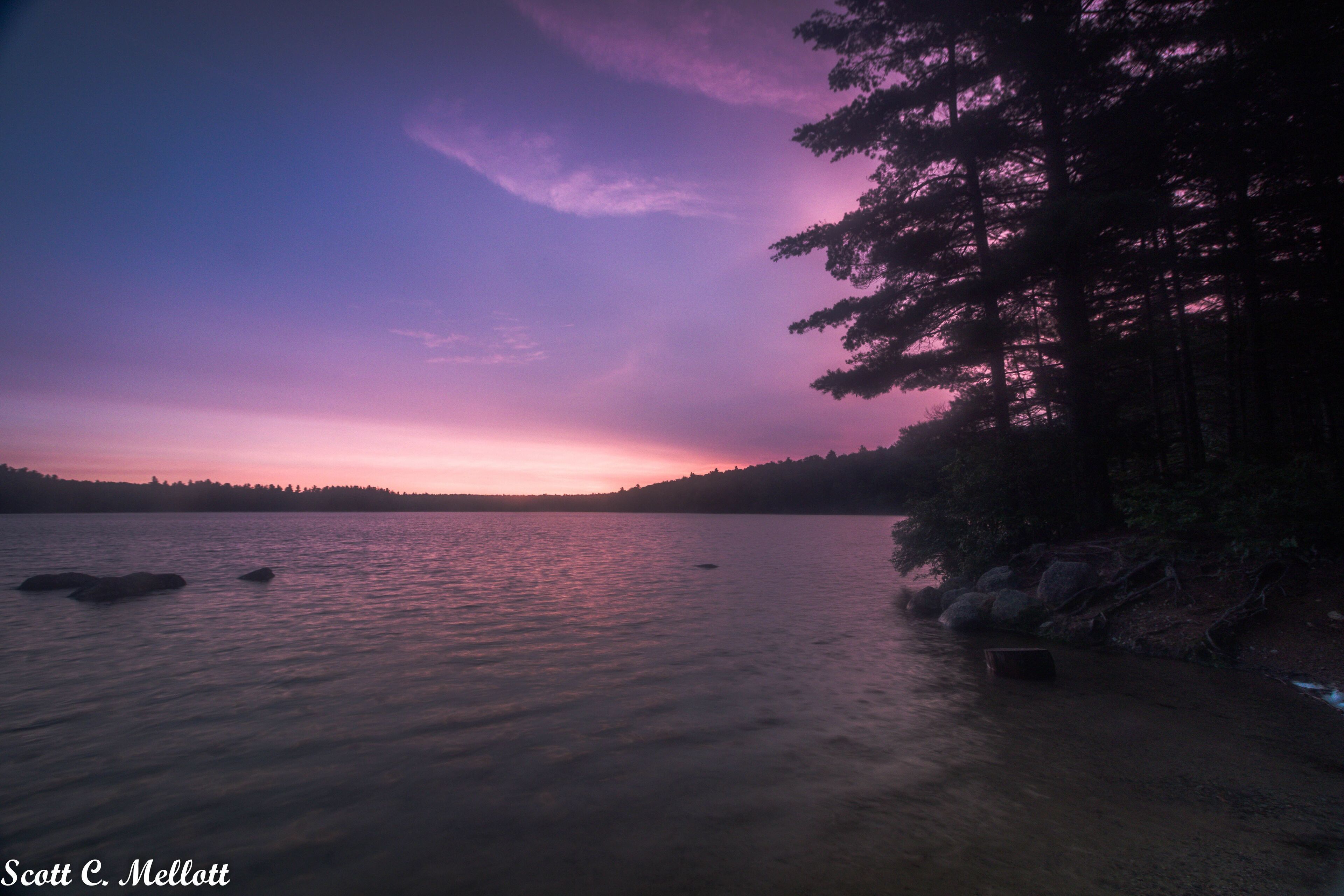 A sunset over a calm lake with a forested shoreline.