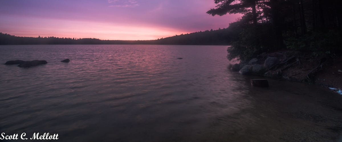 A sunset over a calm lake with a forested shoreline.