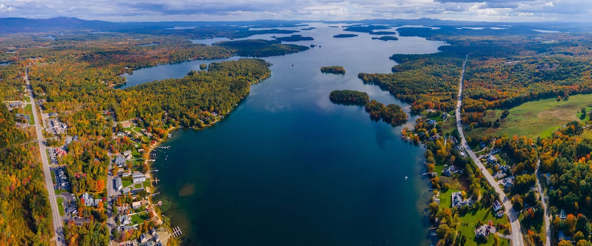 An aerial view of a lake surrounded by autumn-colored forests and residential areas.