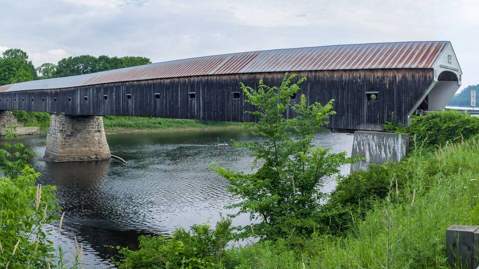 A covered wooden bridge over a river, surrounded by greenery.
