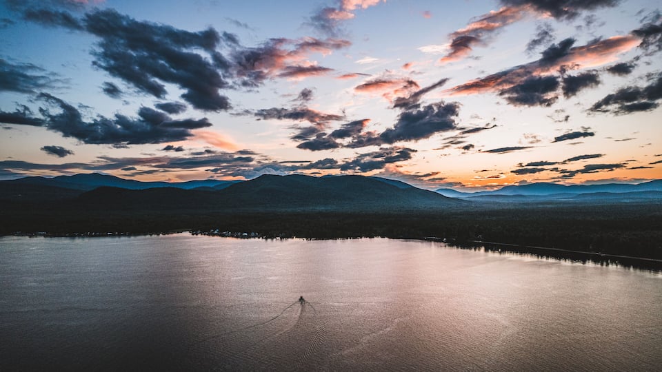 A calm lake with mountains in the background and a sunset sky.