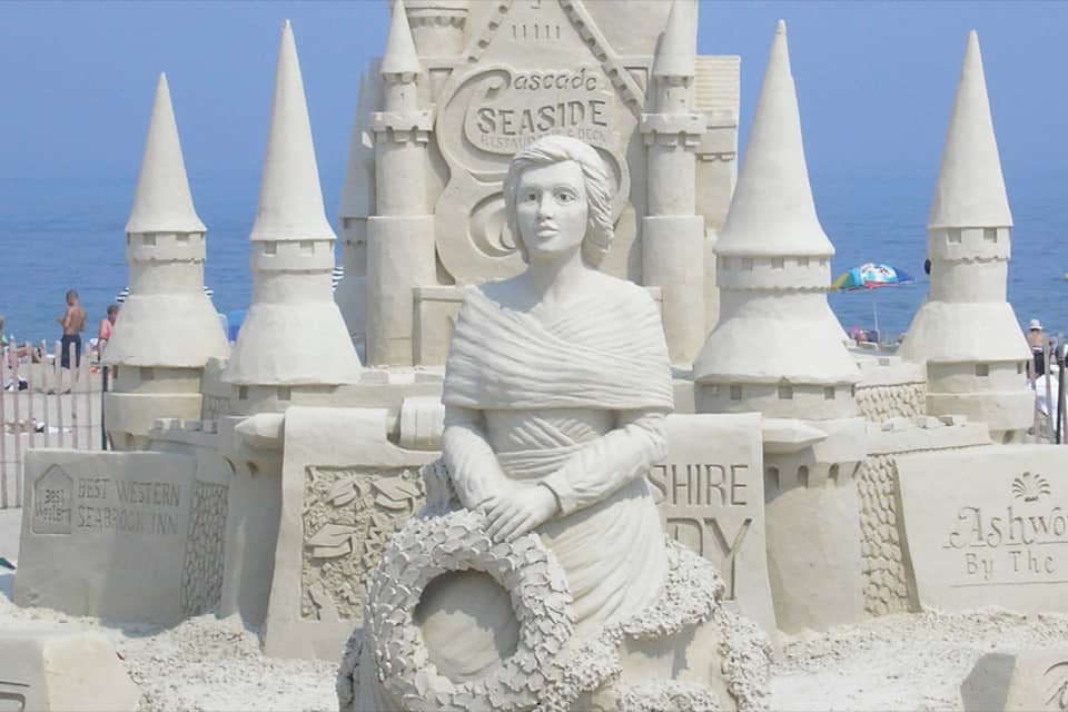 A detailed sandcastle with a central figure, multiple spires, and text indicating 'Seaside' and 'Ashworth By The Sea'.
