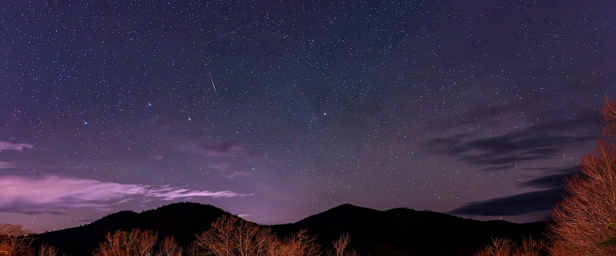 A night sky filled with stars, a row of wooden chairs, and a mountain in the background.