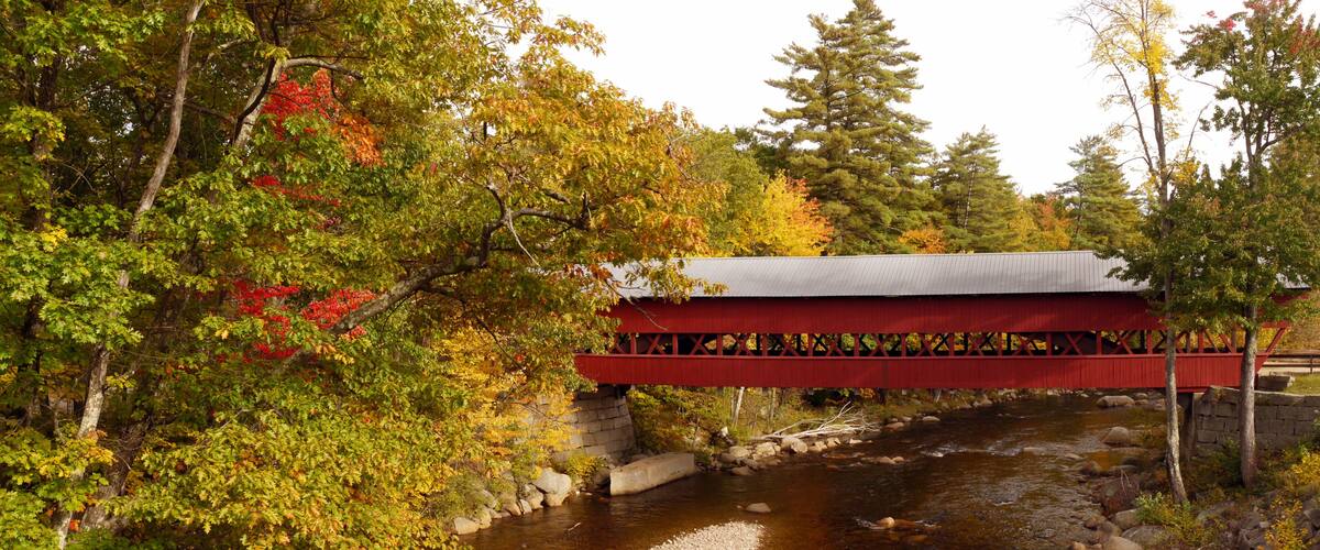 A red covered bridge over a river with autumn foliage.