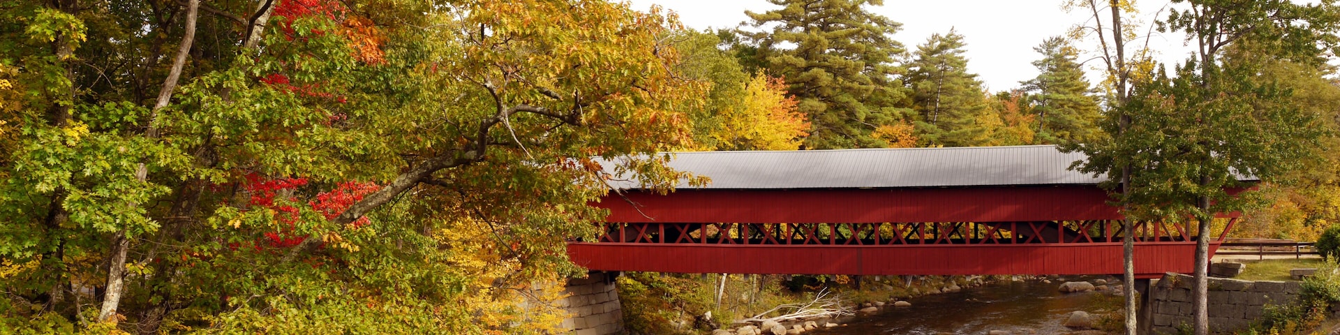 A red covered bridge over a river with autumn foliage.