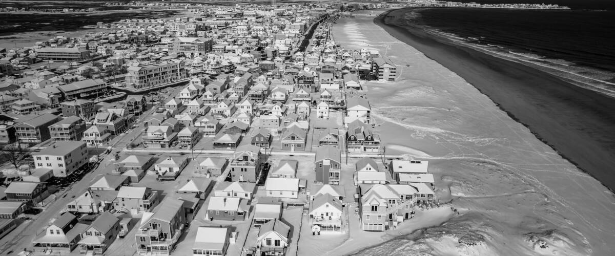 An aerial view of a coastal town with a beach, residential buildings, and a lighthouse in the distance.