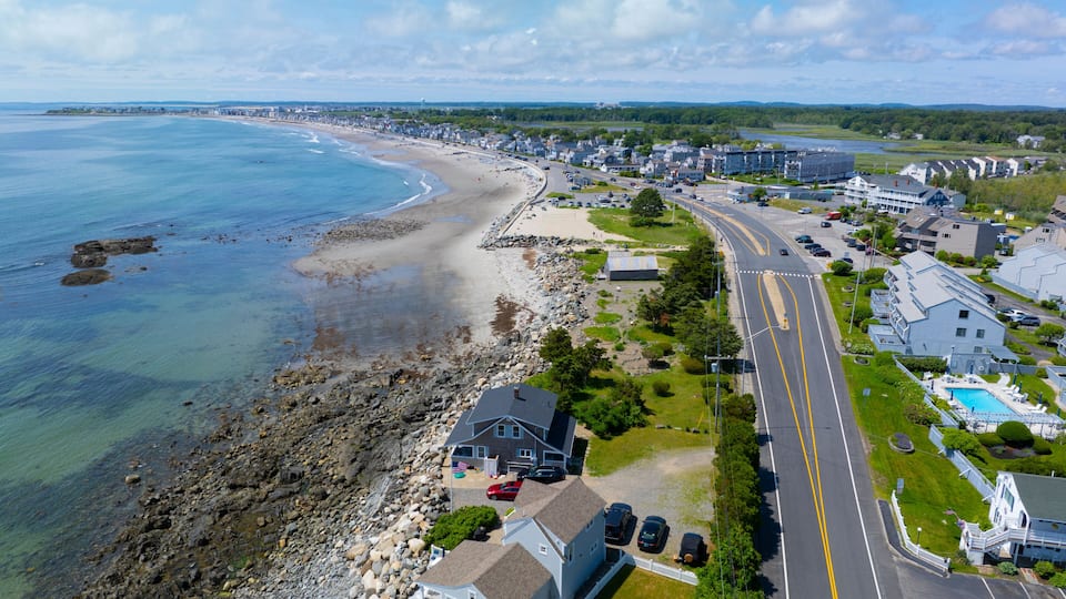 A coastal town with a beach, a road, and residential buildings.
