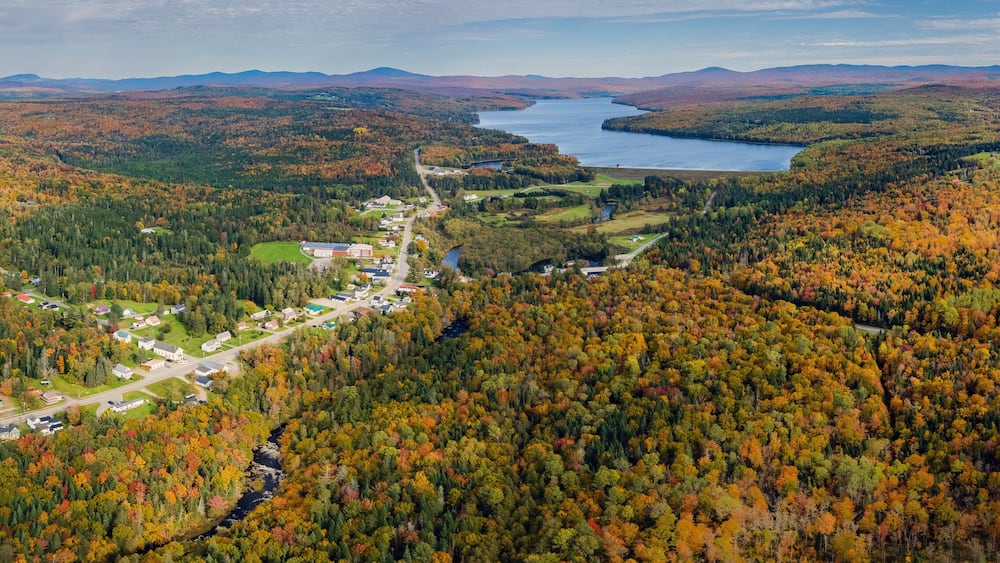An aerial view of a town nestled in a valley with a lake and mountains in the background.